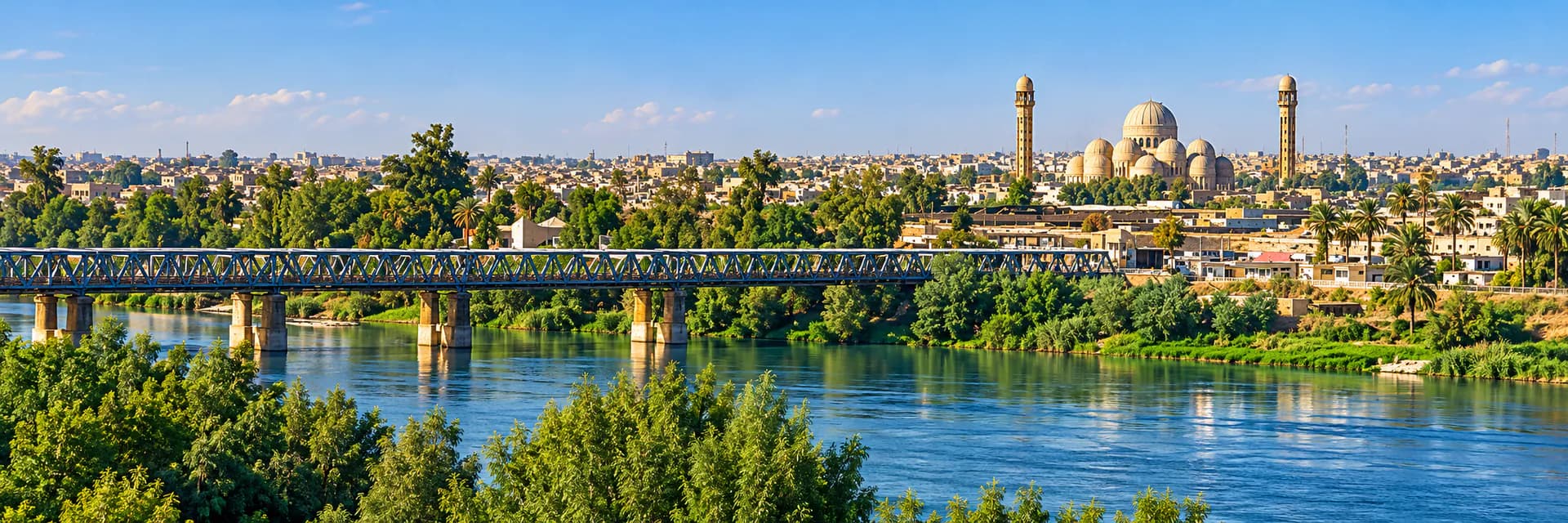 جسر حديدي فوق نهر دجلة في الموصل وخلفه جامع بقبابه ومئذنتيه